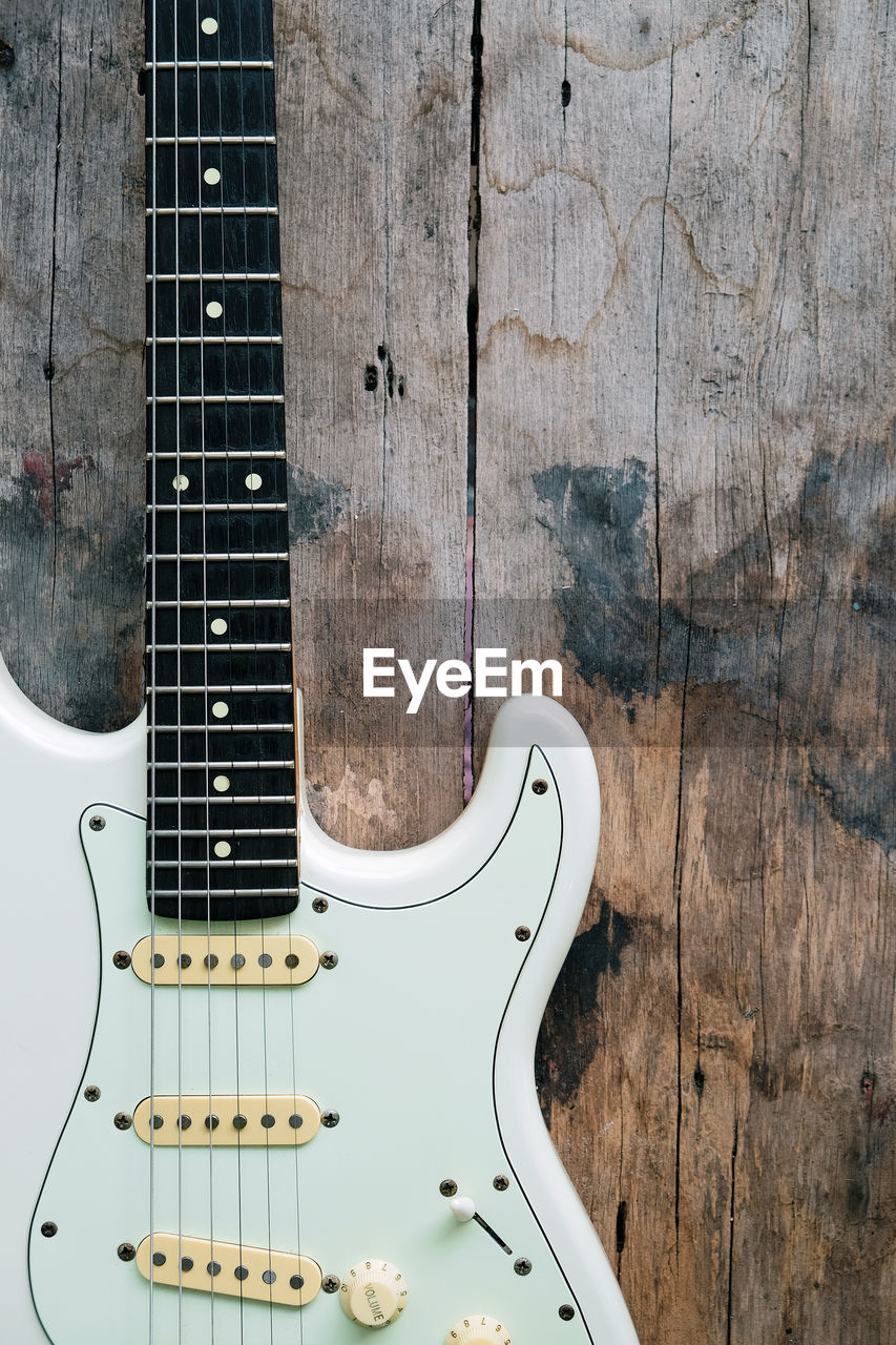 Detail of white electric guitar on a wood background.