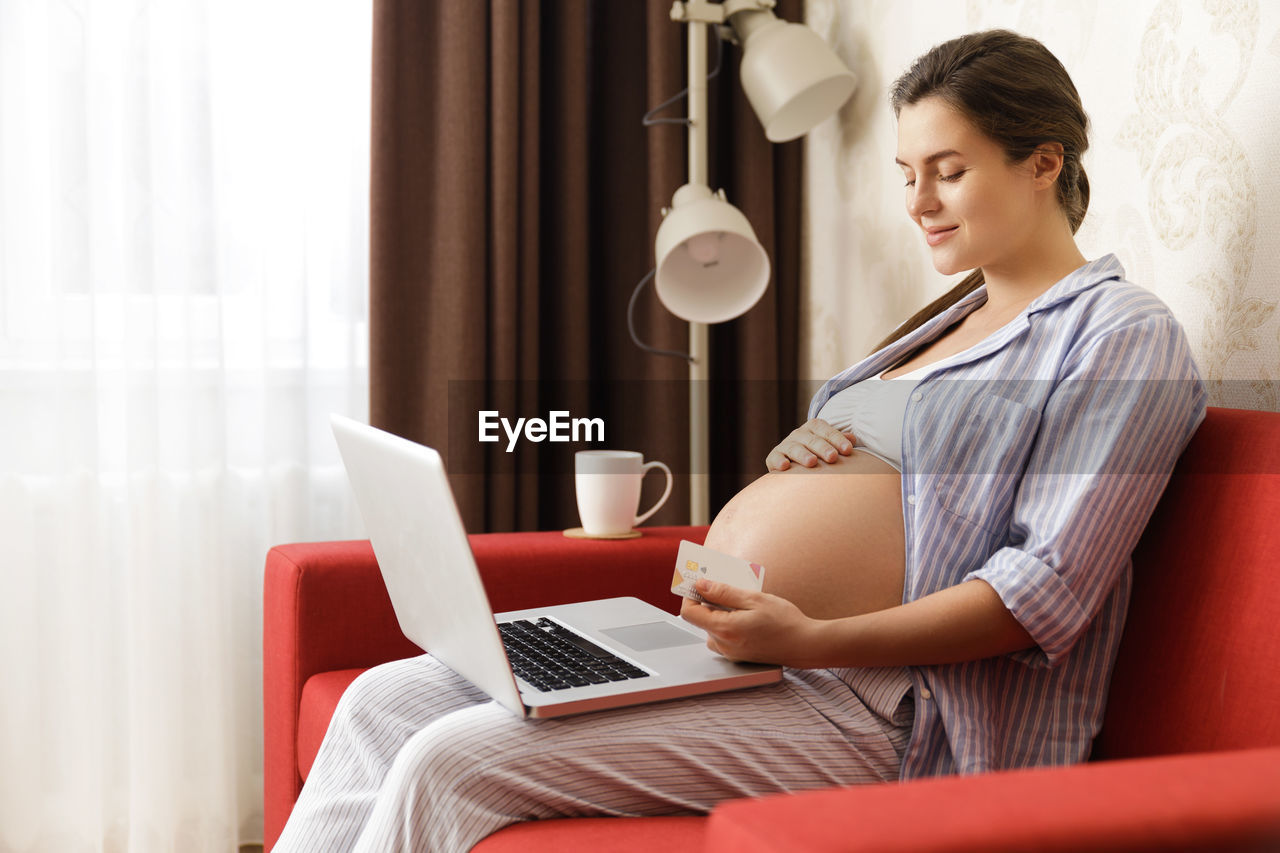 Pregnant woman with laptop sitting on sofa at home