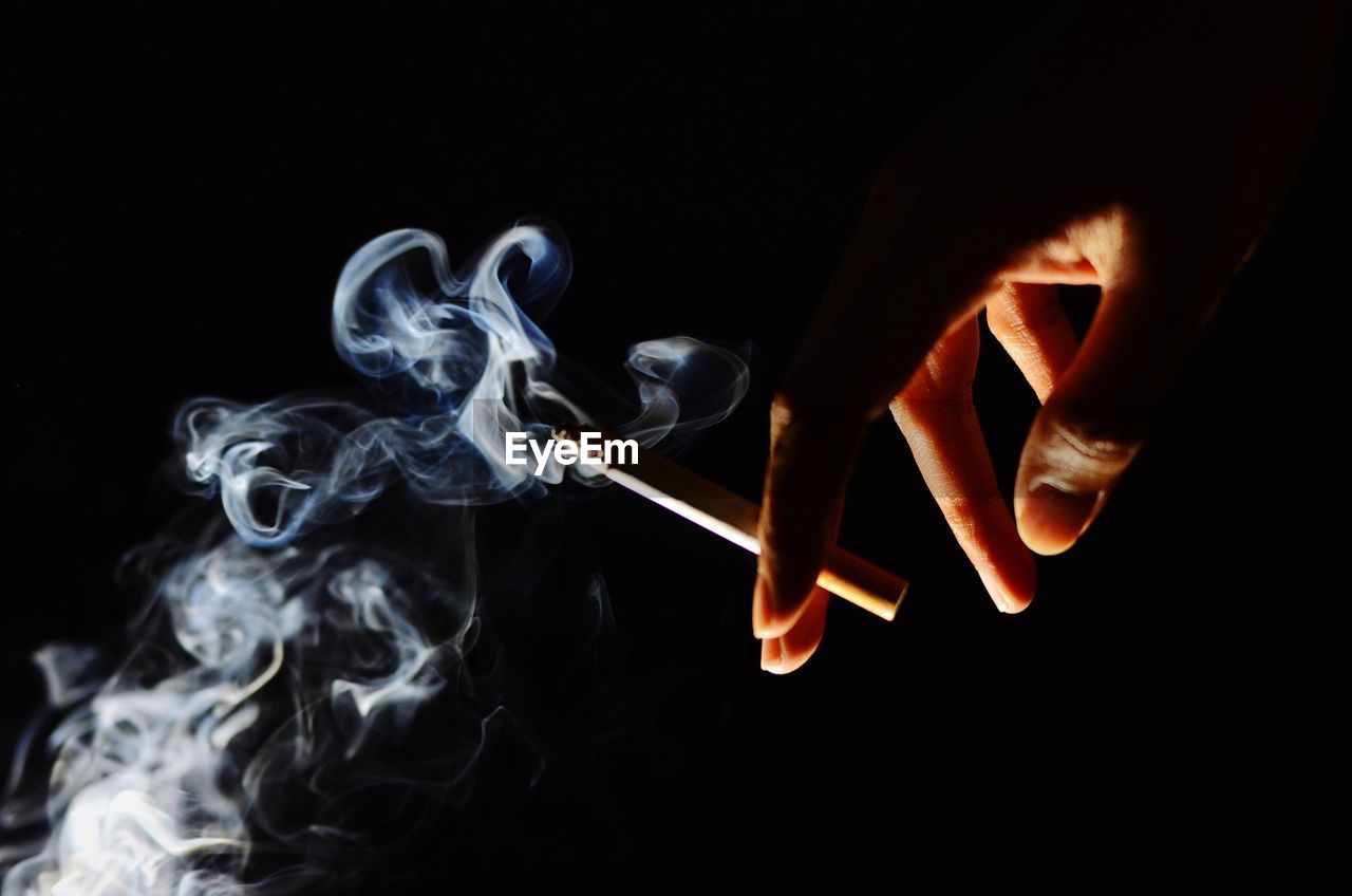 Cropped image of hand holding cigarette against black background