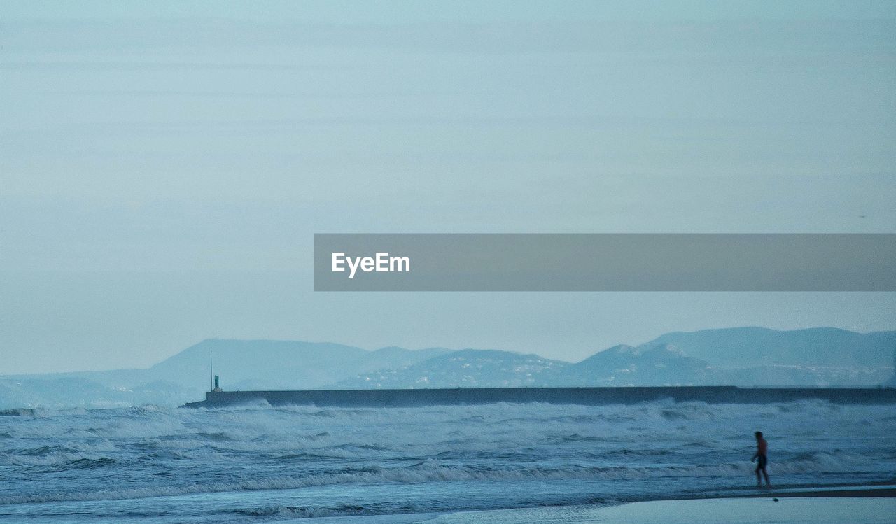 Silhouette man standing at beach against clear sky