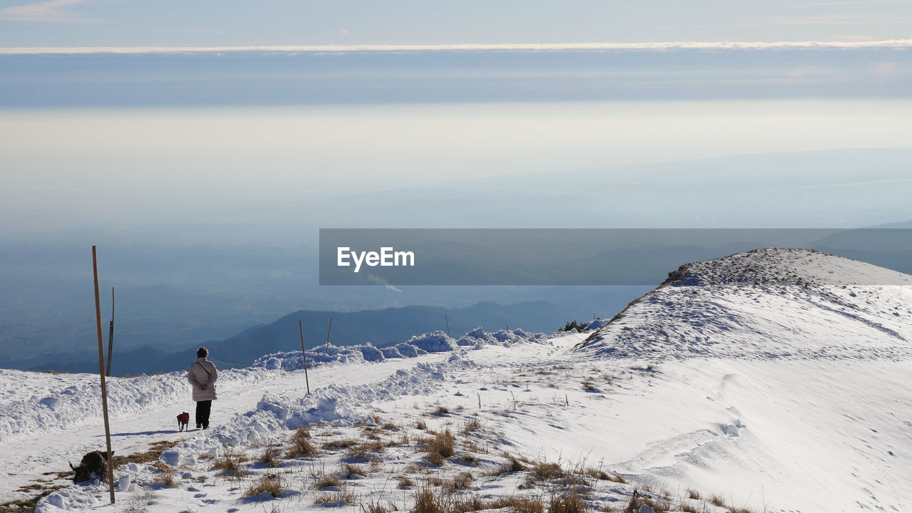 WOMAN ON SNOW COVERED MOUNTAIN AGAINST SKY