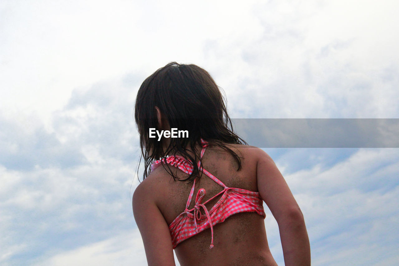 Rear view of girl in bikini standing against sky