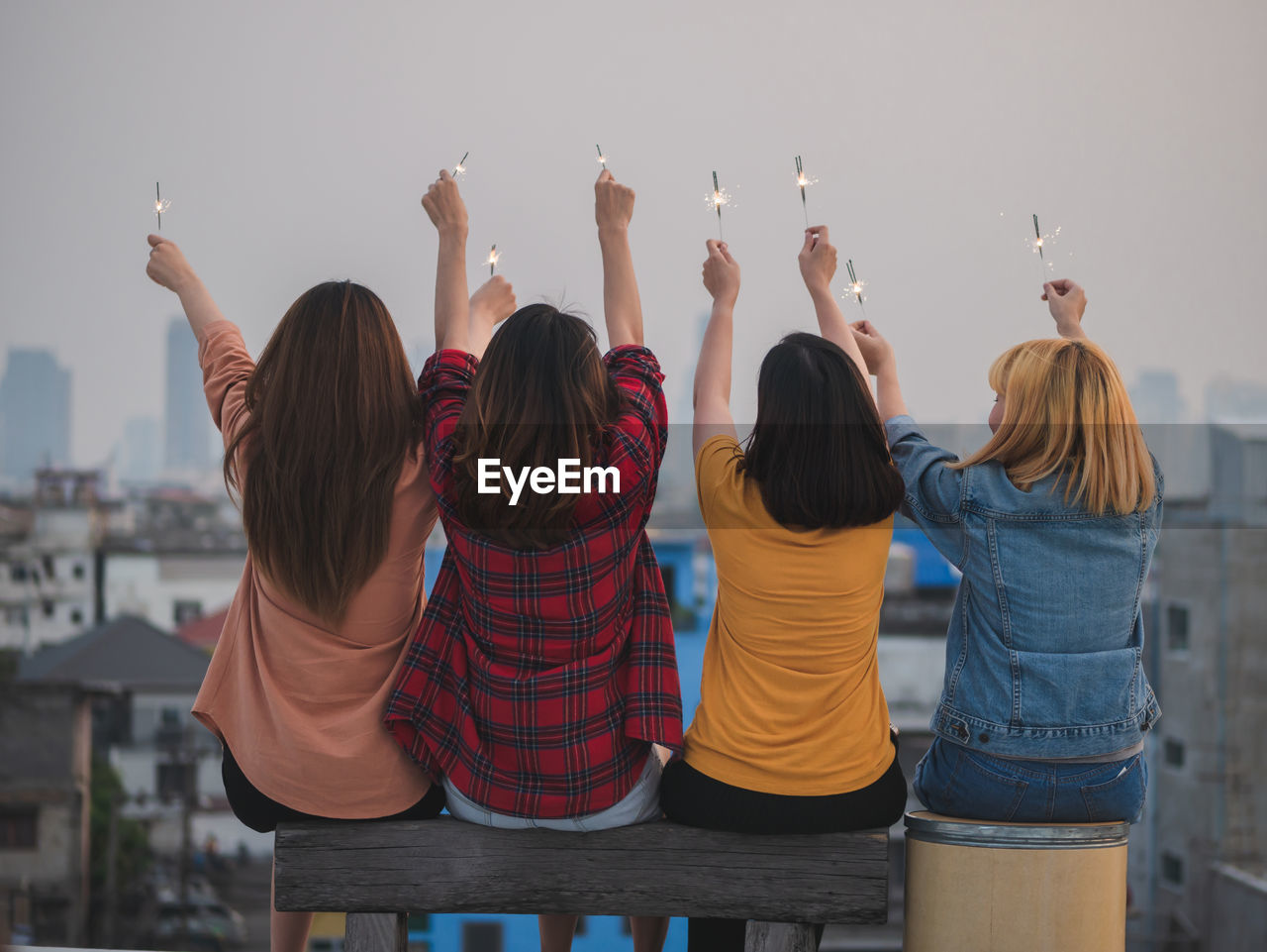 Female friends holding lit sparklers against sky