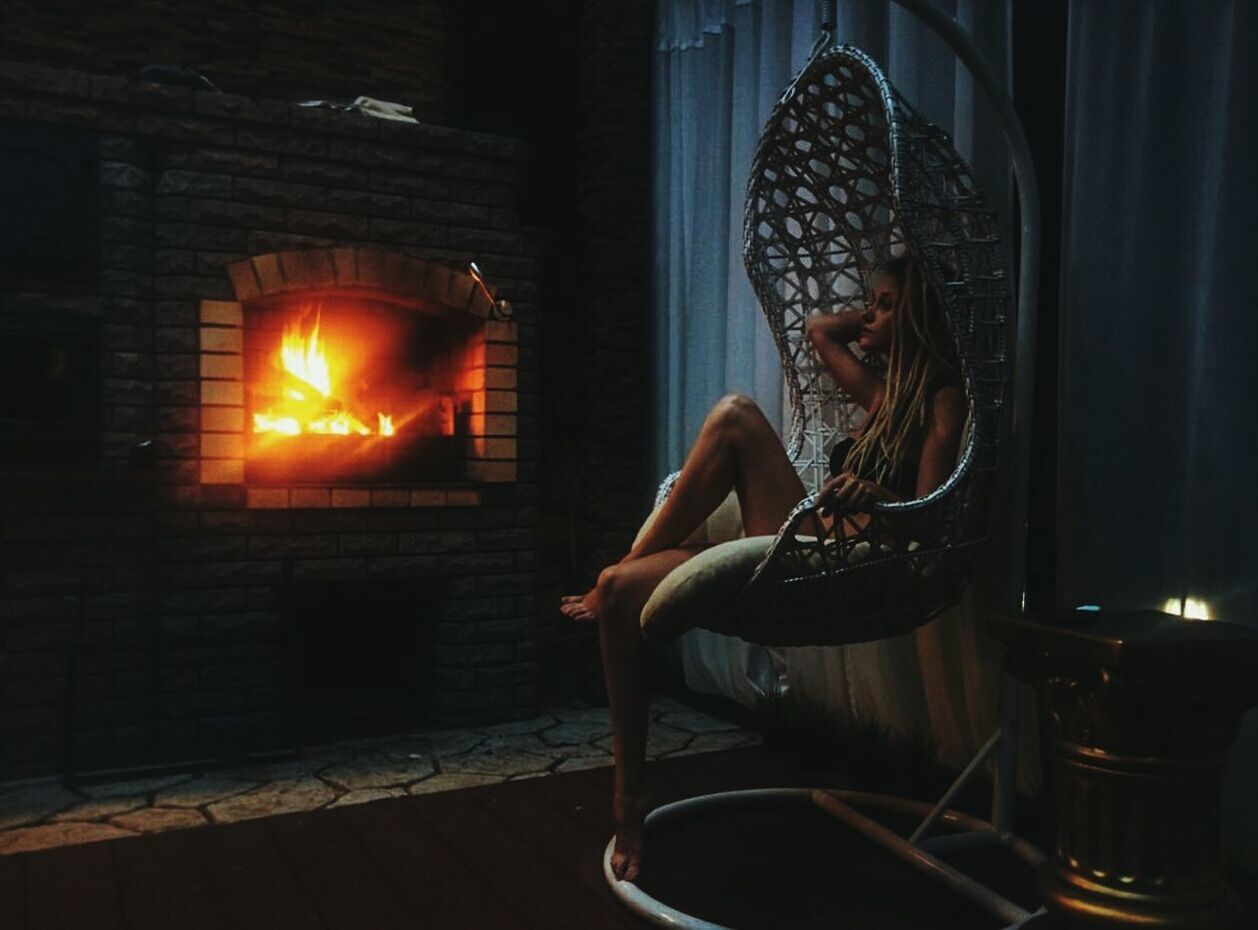 Full length of sensuous woman sitting in swing by fireplace at home