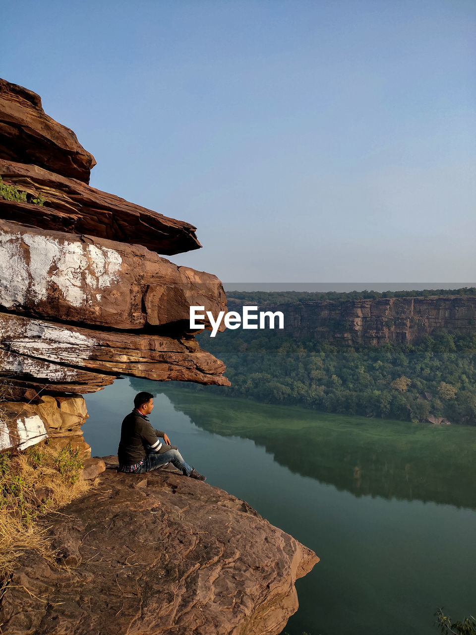 Portraits- man sitting on rock by mountain against sky