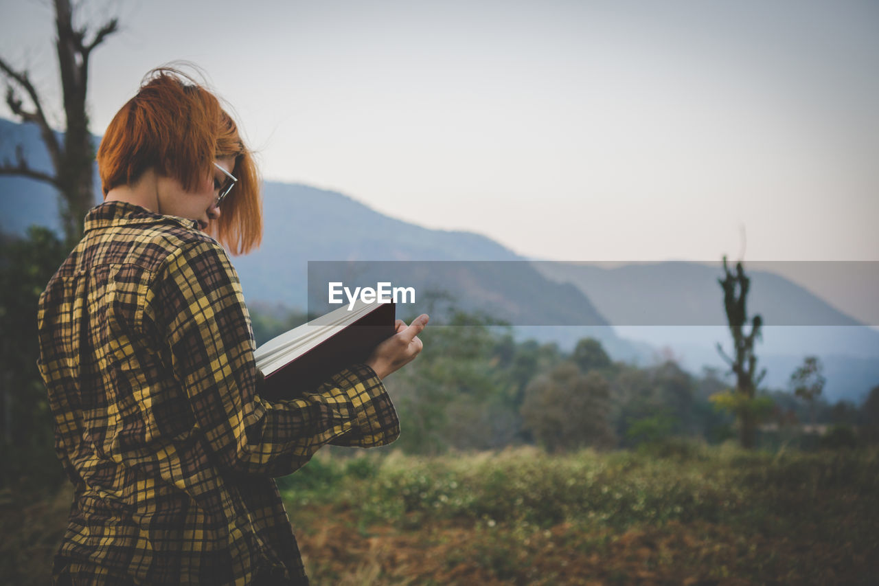 Young woman sitting reading a book at nature in the evening.
