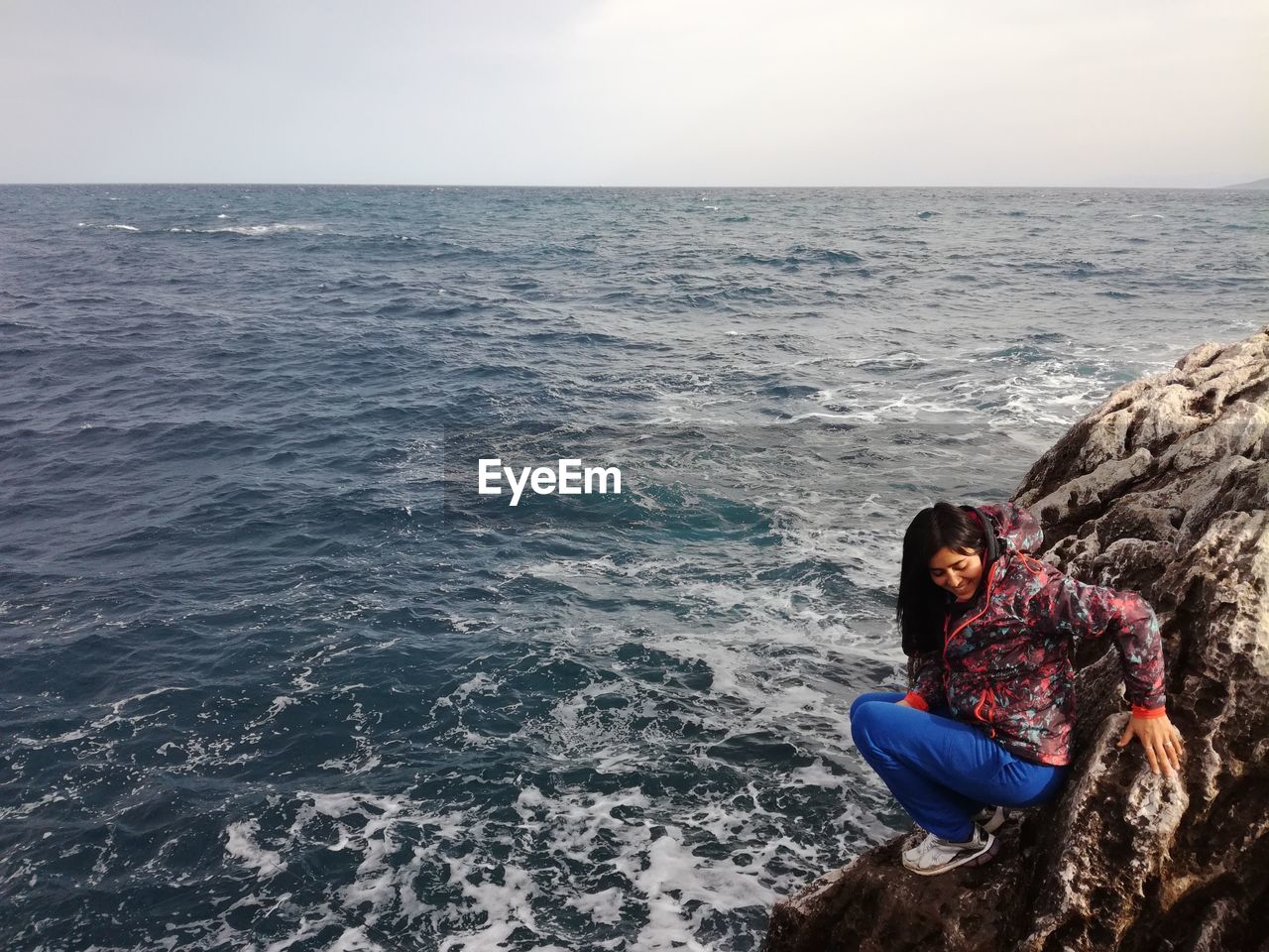 Full length of woman crouching on rock by sea against sky