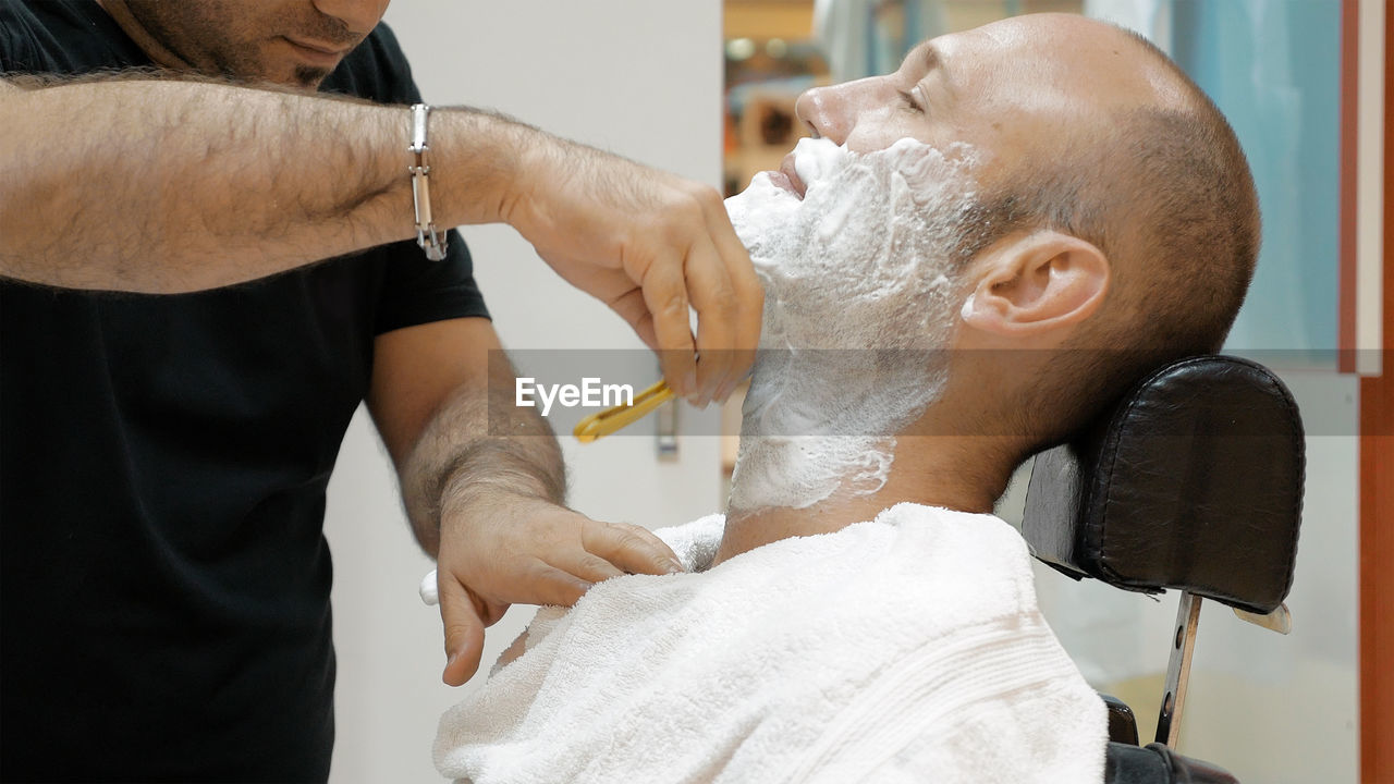 Midsection of barber doing shaving of mature man in salon