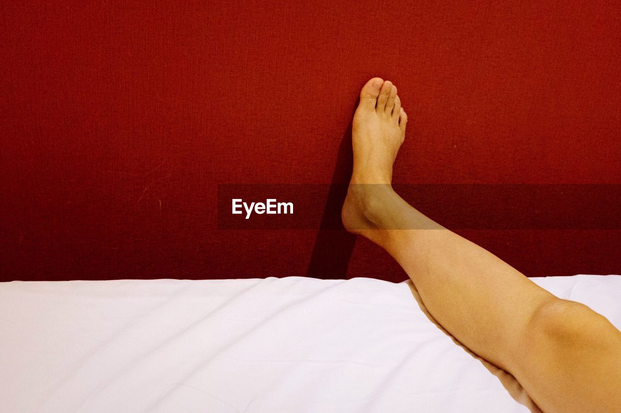 Low section of woman lying on bed by red wall