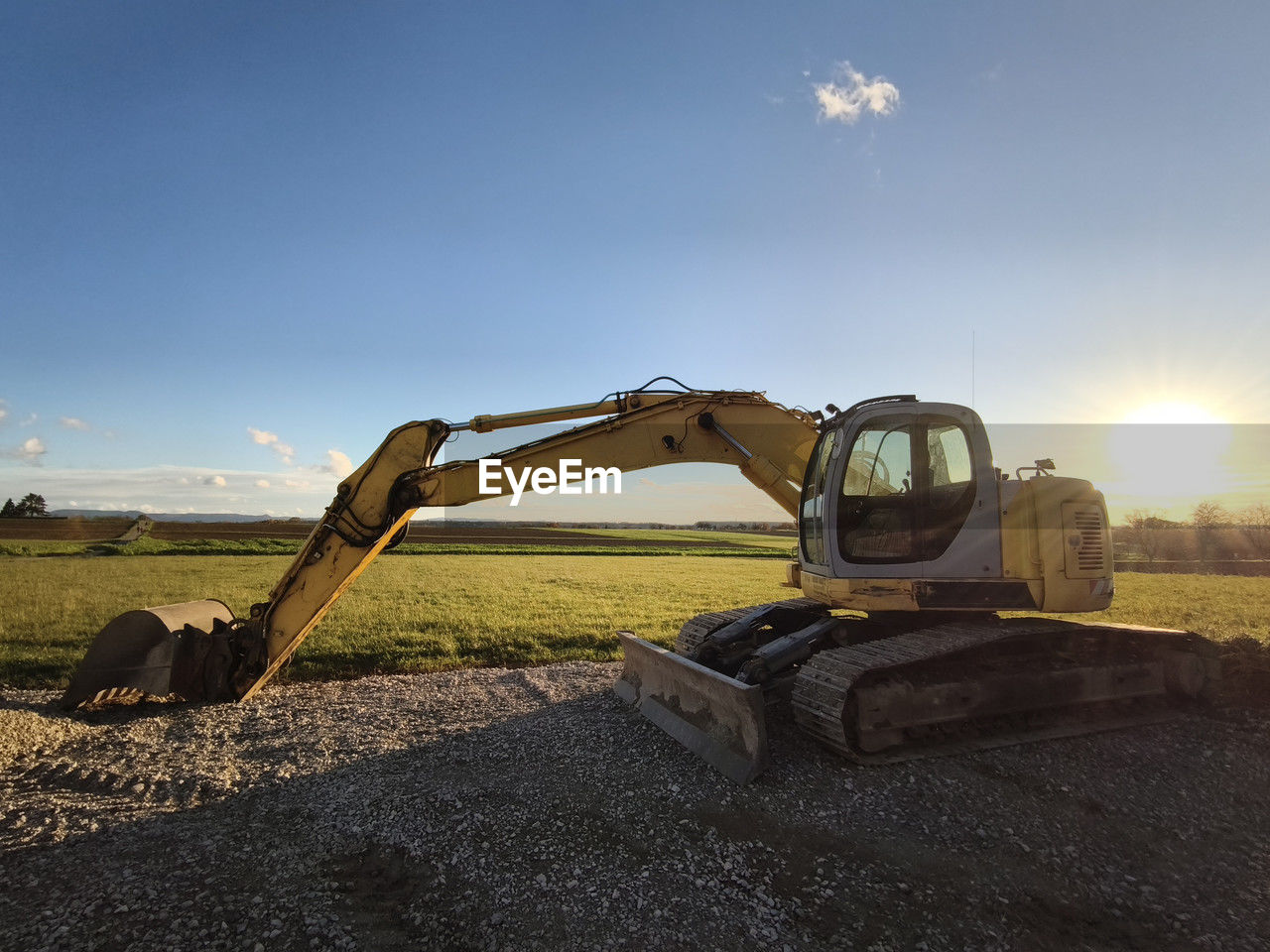 sky, transportation, nature, sunlight, field, machinery, landscape, vehicle, construction machinery, soil, land, mode of transportation, earth mover, sun, construction industry, environment, rural scene, road, agriculture, sand, no people, day, land vehicle, lens flare, outdoors, blue, industry, sunny