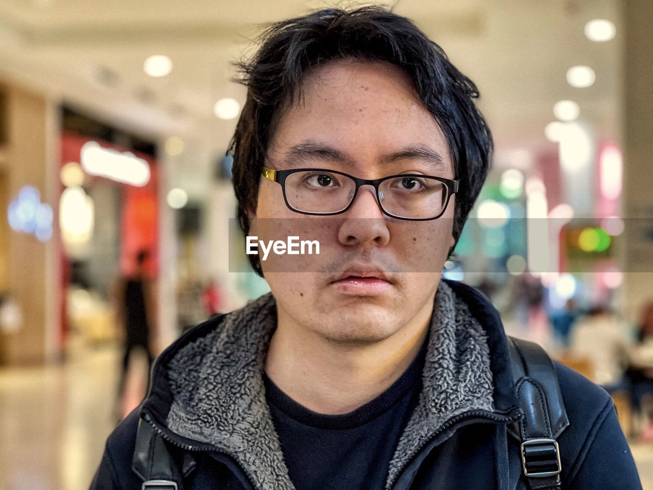 Portrait of young asian man in eyeglasses against illumination inside shopping mall.