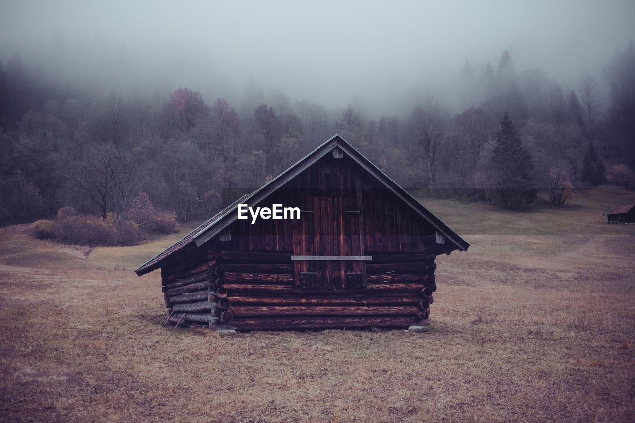 Wooden house on field against trees in forest