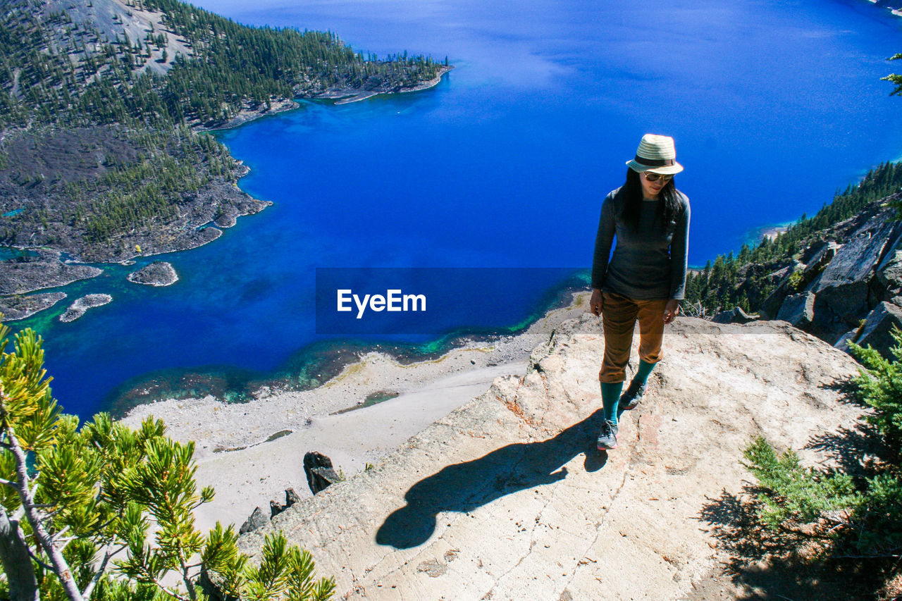 High angle view of young woman standing on cliff by crater lake