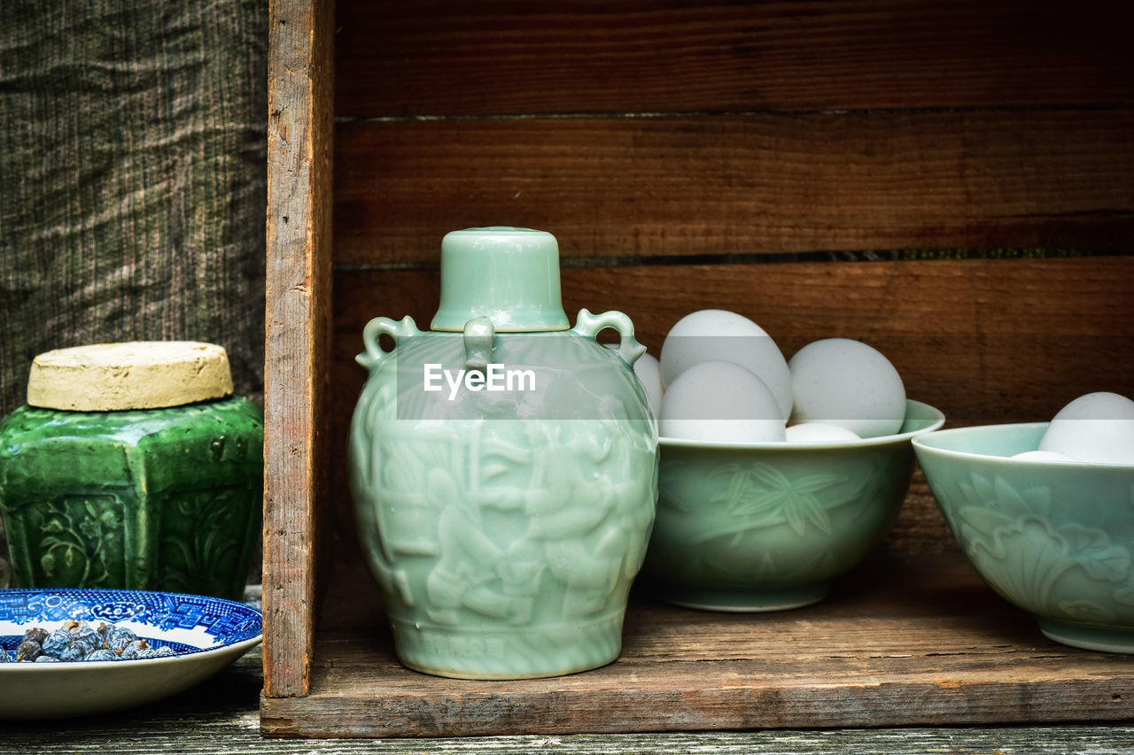 Celadon green ceramic bottle and bowls of eggs in vintage wooden box still life