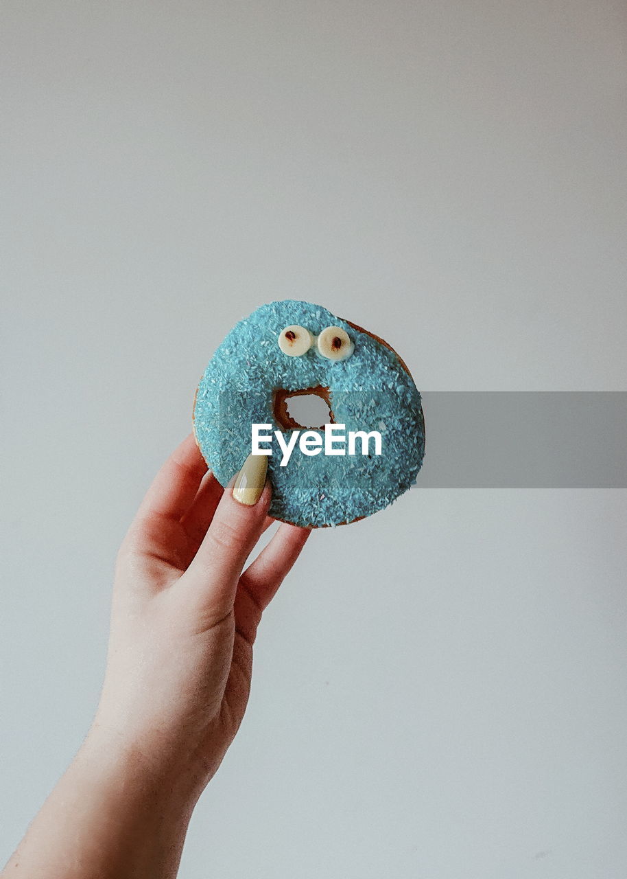 Cropped hand of woman holding donuts against gray background