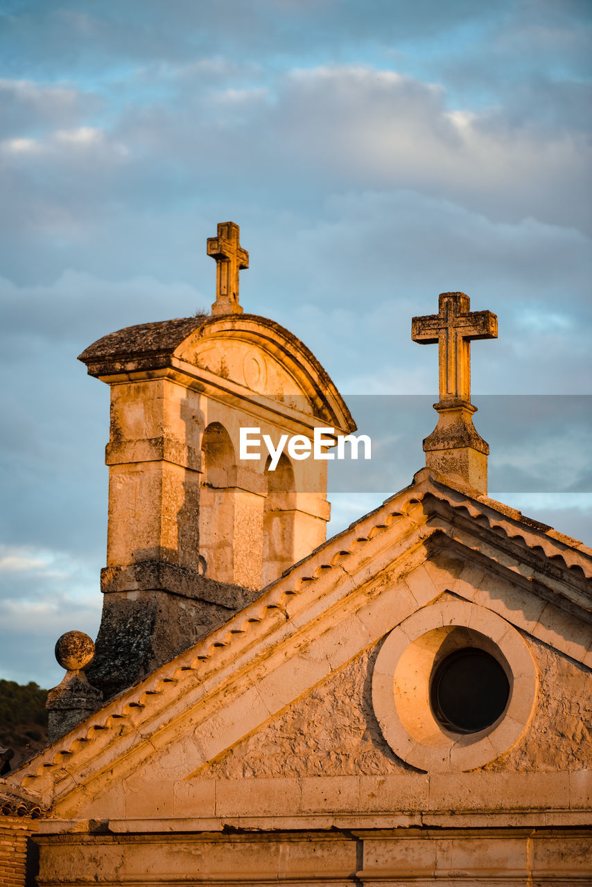 Low angle detail of medieval stone church building with crosses on top against cloudy sky in cuenca town in spain