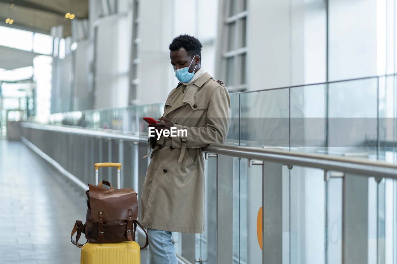 Man wearing mask using smart phone at airport