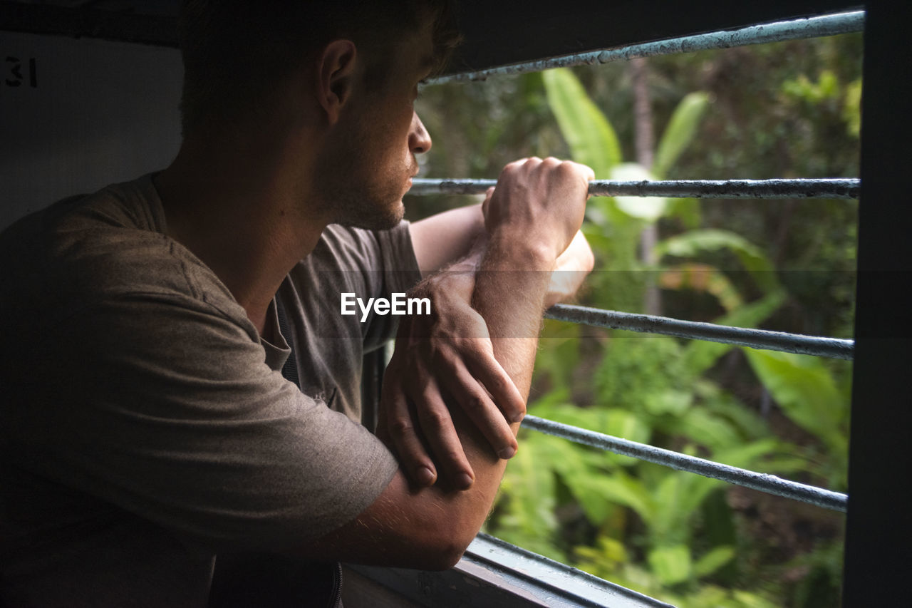 Side view of man looking at plant through train window