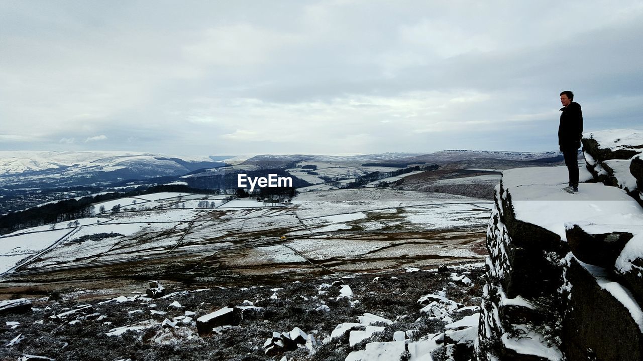 Man standing on snow covered cliff against sky