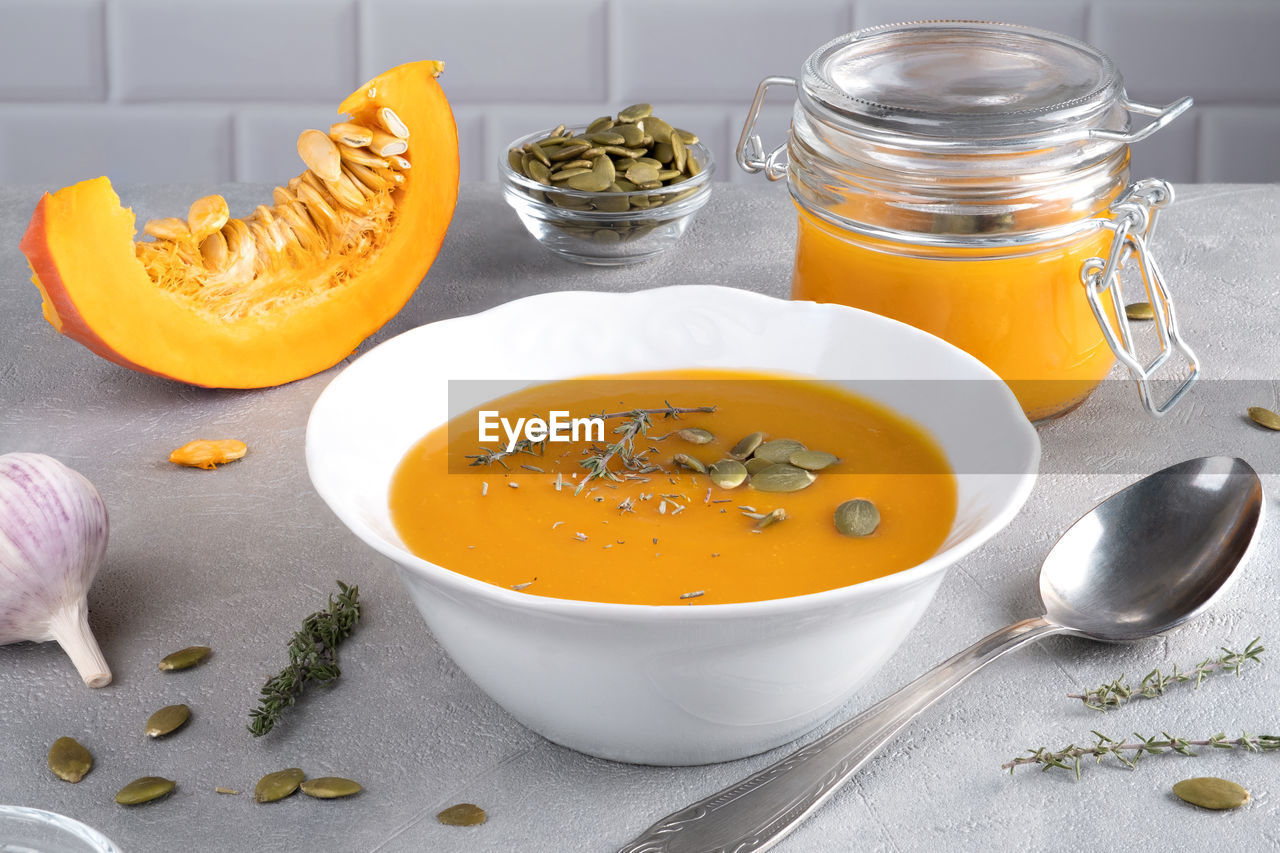 Pumpkin puree soup with pumpkin seeds and thyme in a white plate and glass jar. healthy diet. 