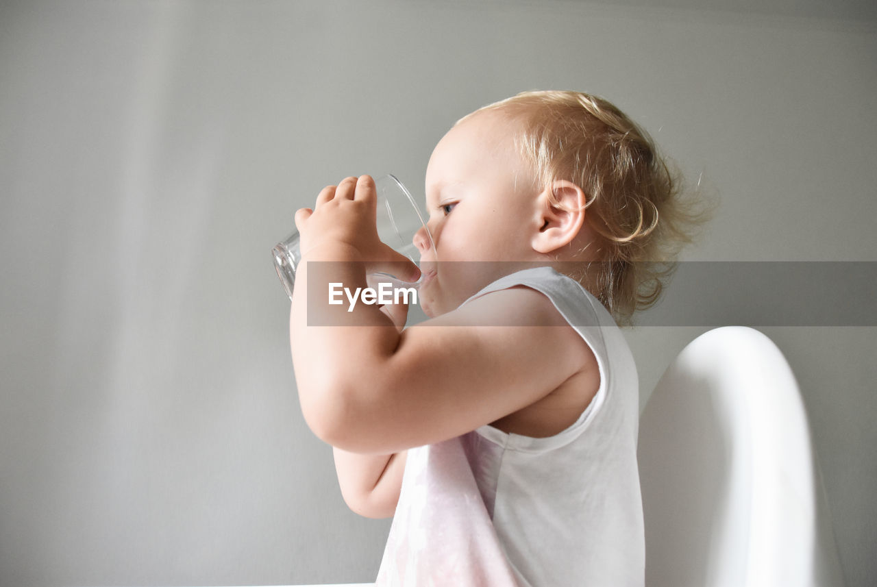 Cute baby girl  against white background drinking water 