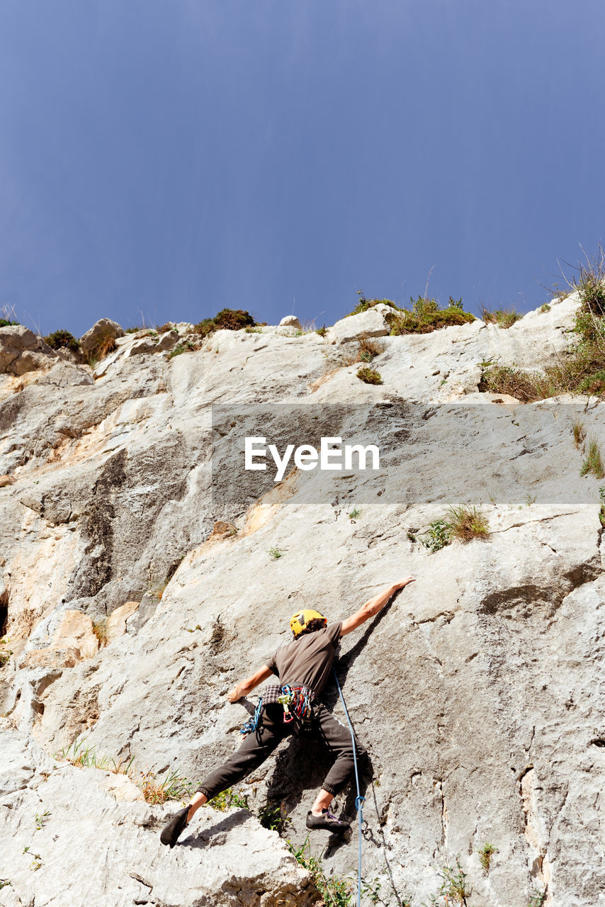 Sportive male alpinist climbing on sheer cliff in summer day