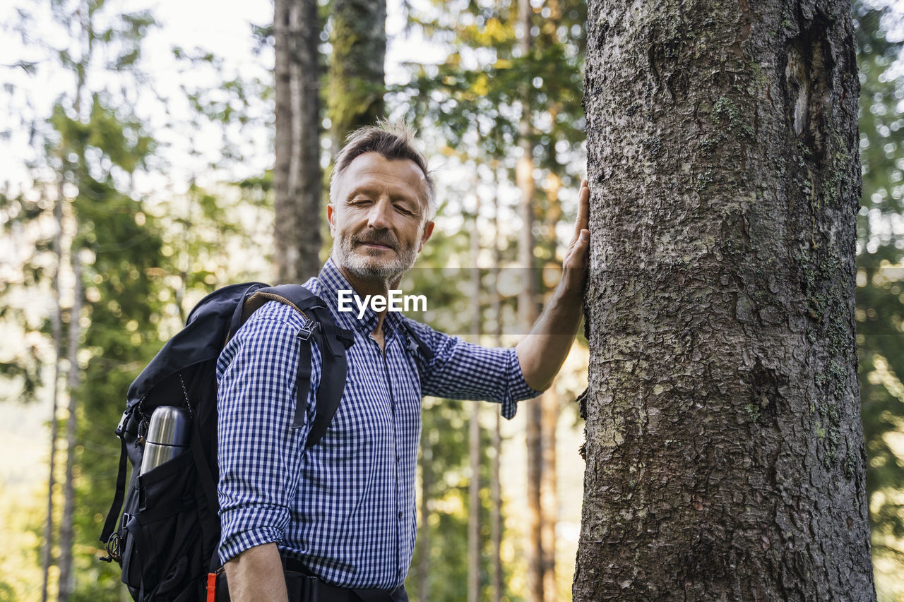 Male hiker with backpack touching tree trunk