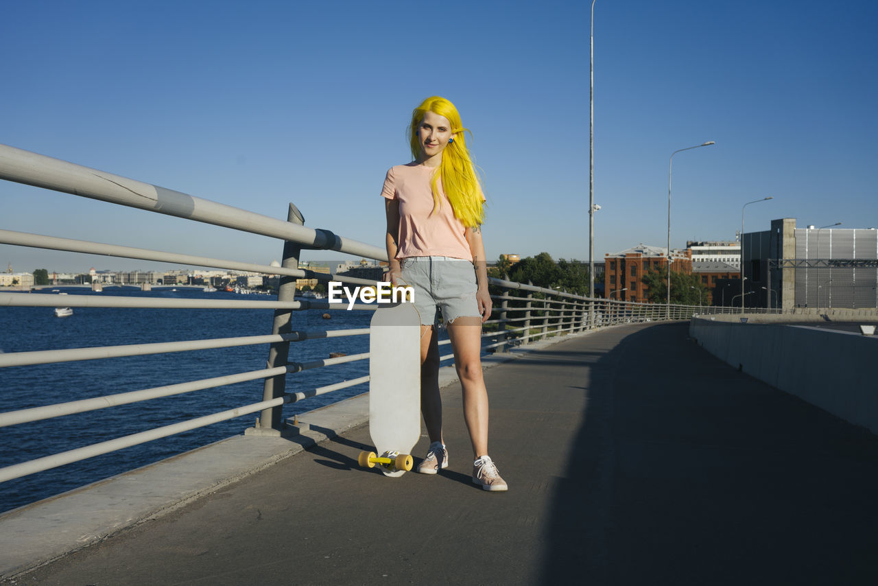 Young woman standing with skateboard on bridge during sunny day