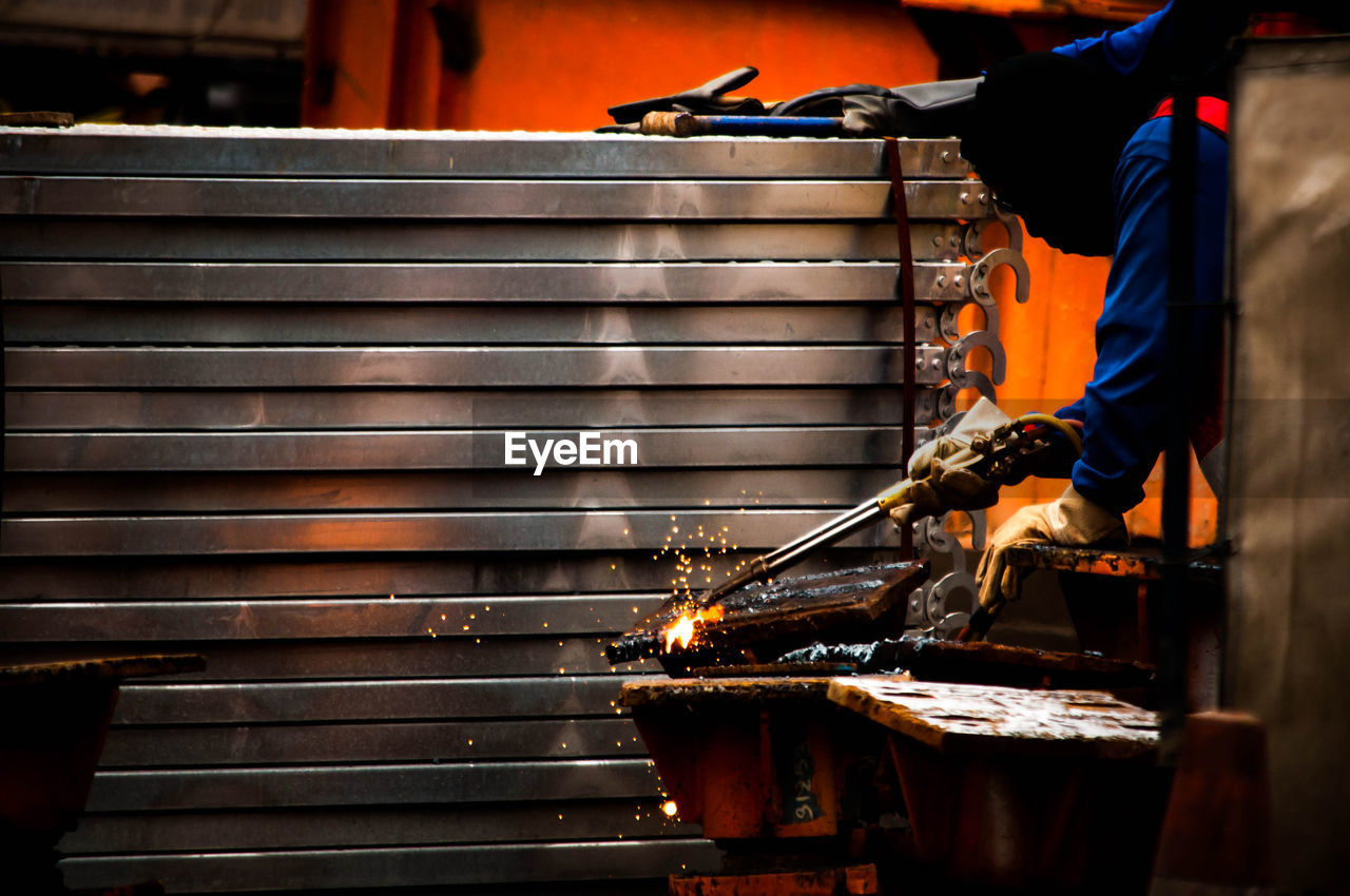 REAR VIEW OF MAN WORKING ON METAL