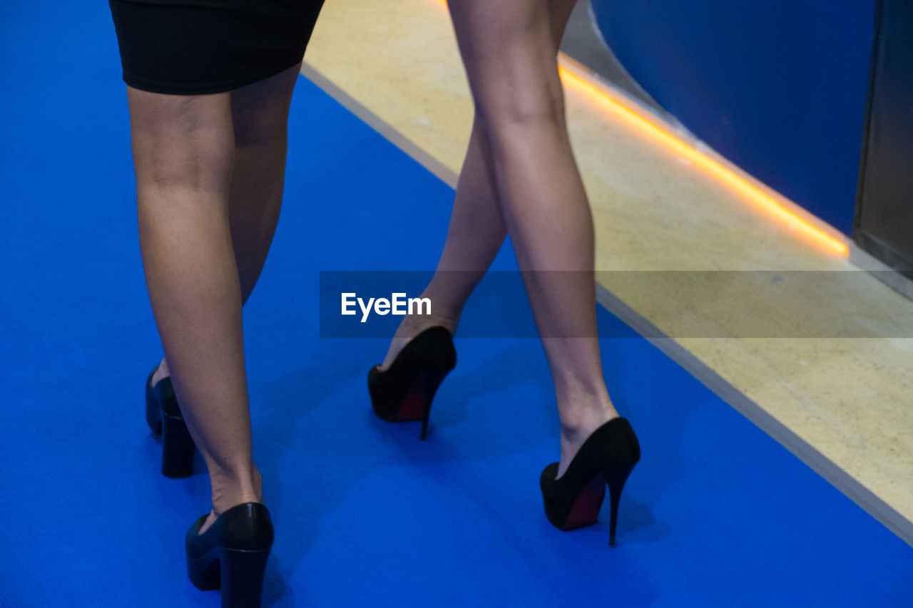 LOW SECTION OF WOMAN WEARING HIGH HEELS AT BLUE