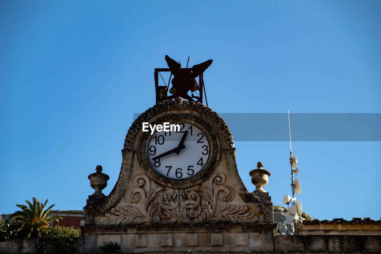 clock, architecture, time, landmark, sky, built structure, clear sky, blue, building exterior, clock face, no people, travel destinations, nature, clock tower, history, monument, statue, city, the past, sculpture, tower, building, day, low angle view, representation, travel, outdoors, animal representation, wall clock, sunny