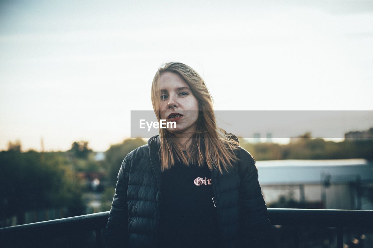 Portrait of young woman standing against sky