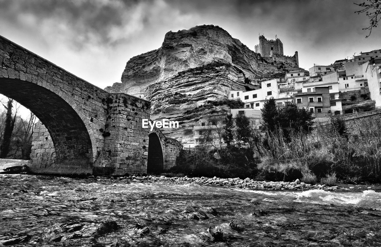 Arch bridge by buildings against sky in city