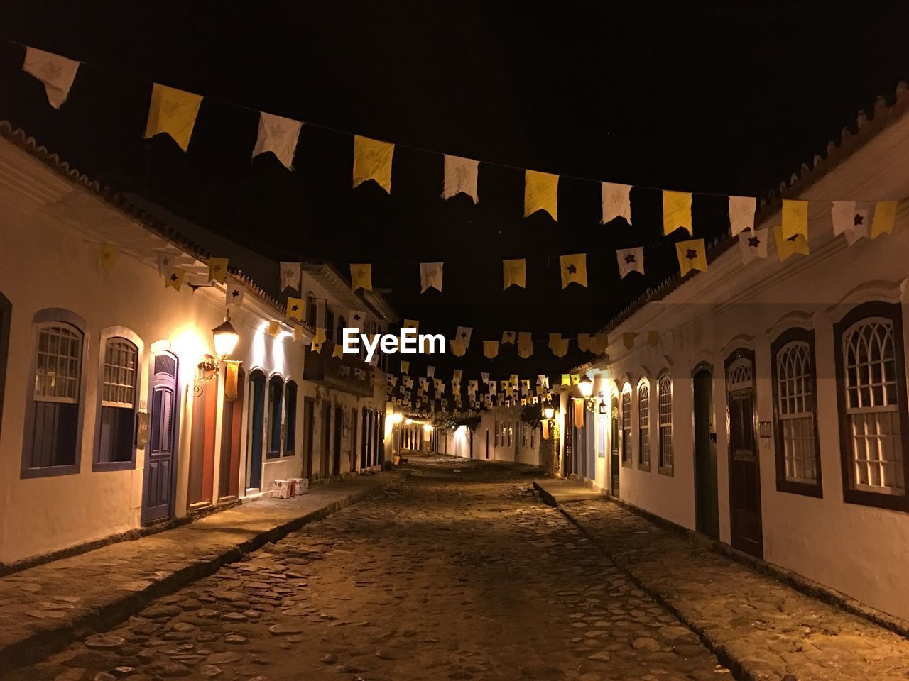 EMPTY ILLUMINATED ALLEY AMIDST BUILDINGS AT NIGHT