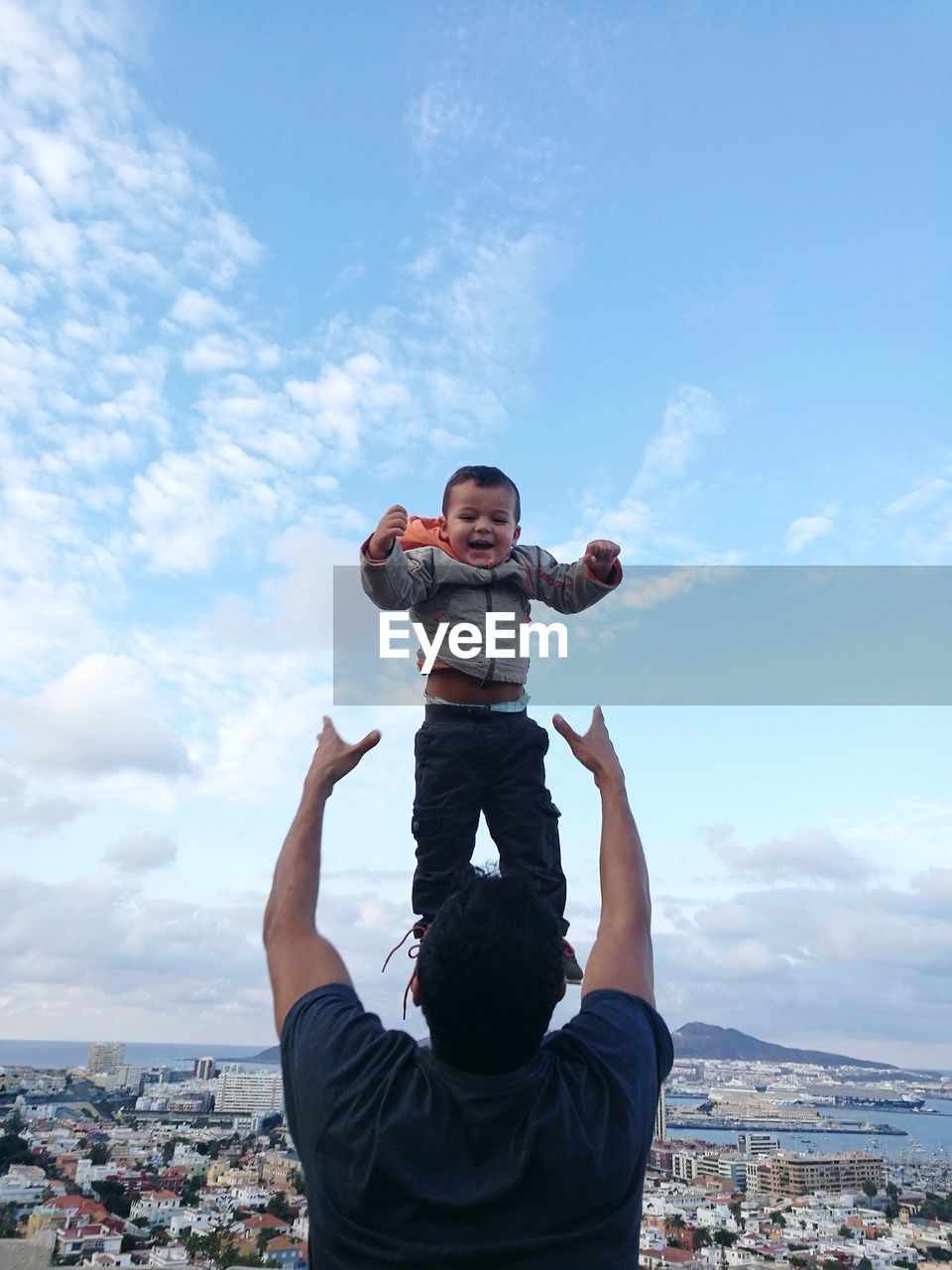 Rear view of playful father throwing son in air against sky