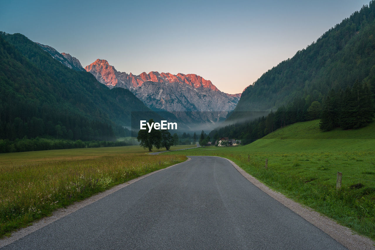 Empty road leading towards mountain against sky