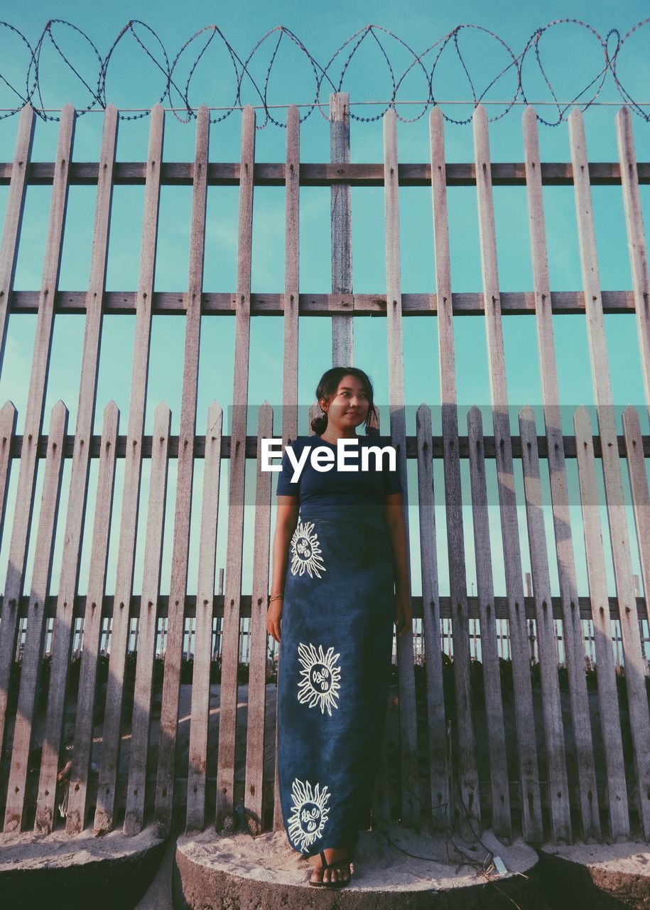 Young woman standing against fence