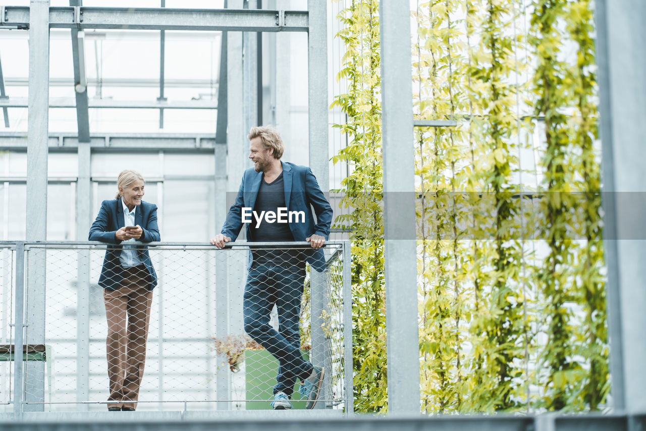 Agronomist discussing with coworker by railing in plant nursery