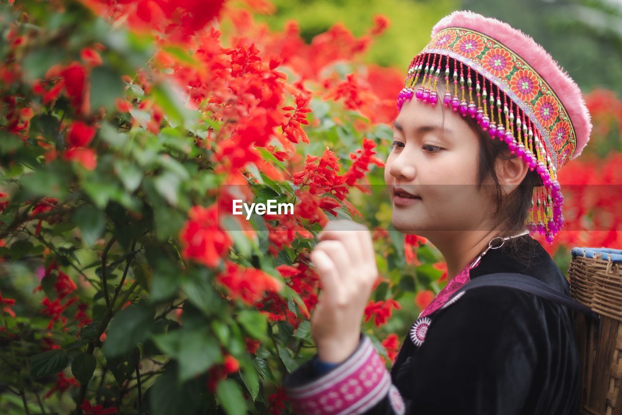 Side view of young woman looking at red flowers