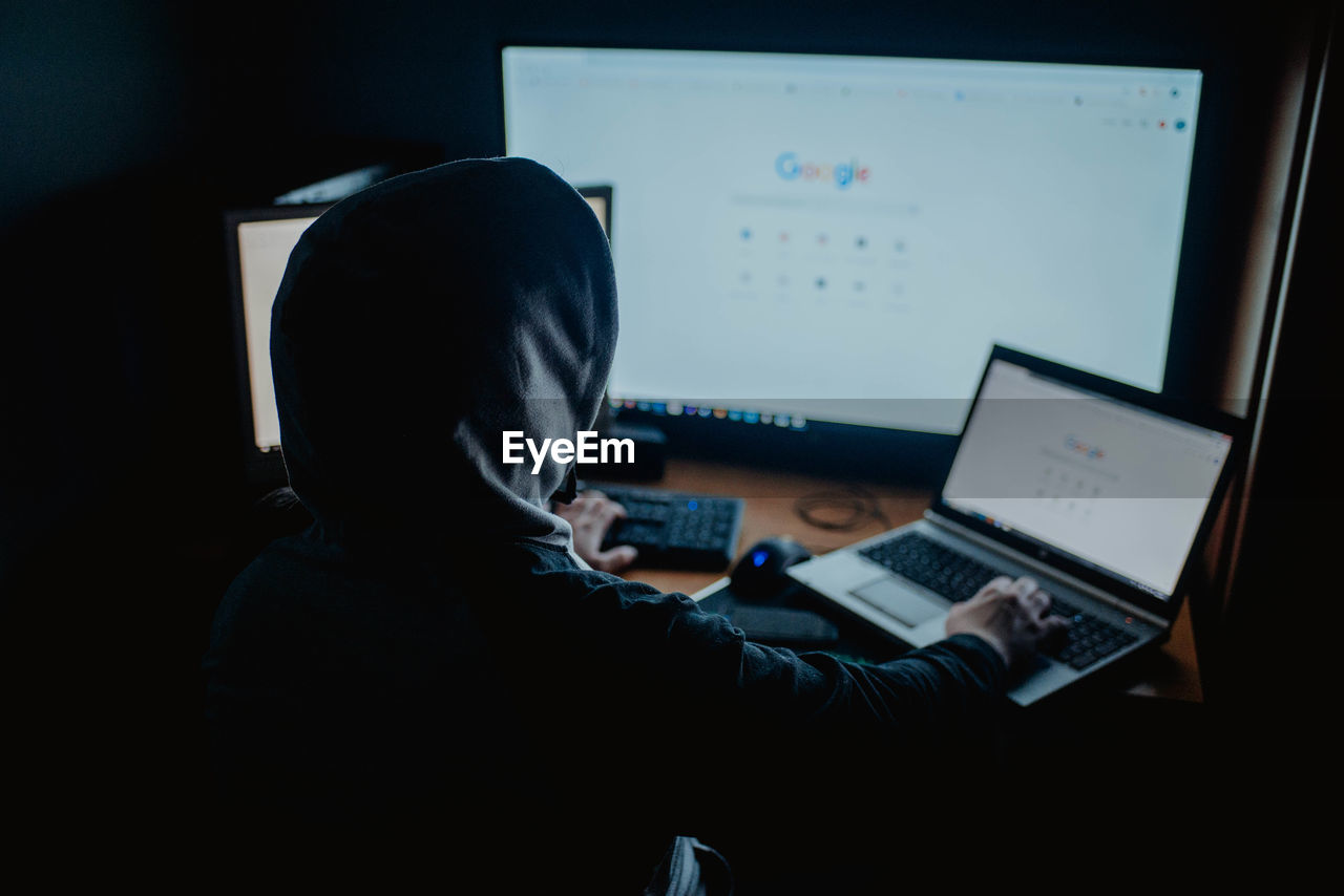 REAR VIEW OF MAN WORKING ON LAPTOP