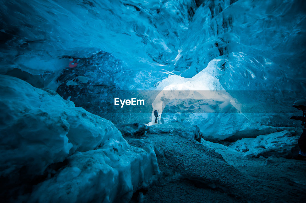 Remote view of traveler standing in ice cave in winter during vacation in iceland