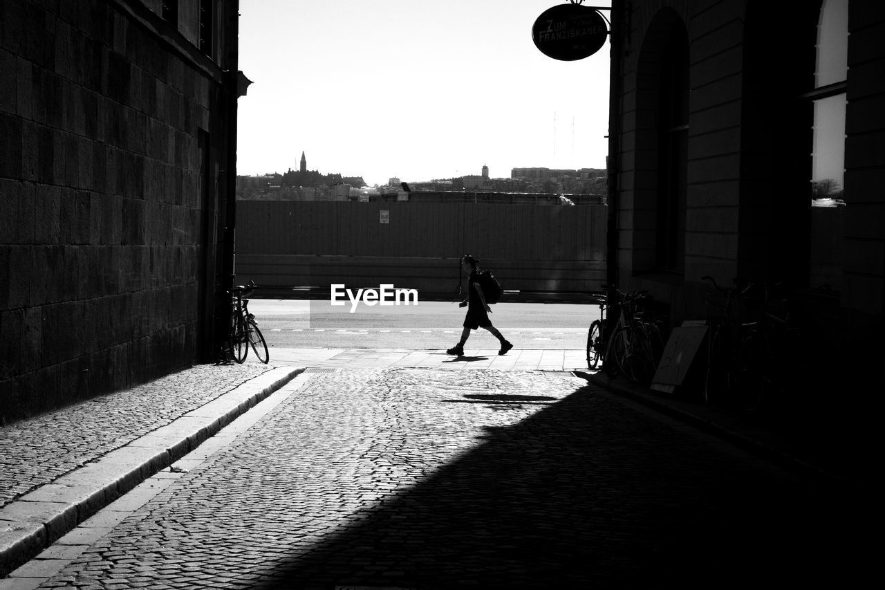 SILHOUETTE MAN WALKING ON STREET BY BUILDINGS