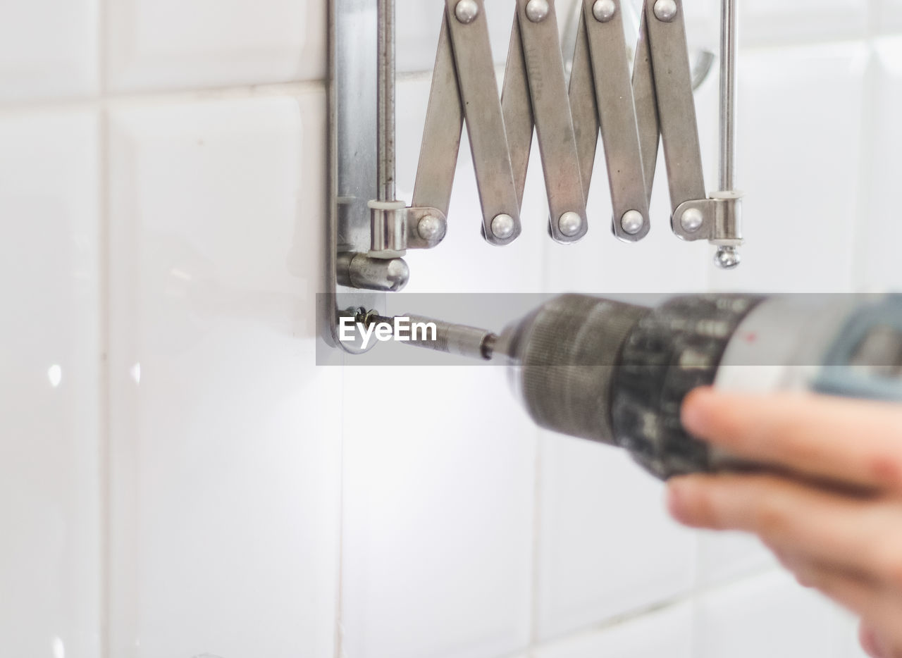 The hands of a young caucasian guy are tightening a screw on a metal fastener using a drill