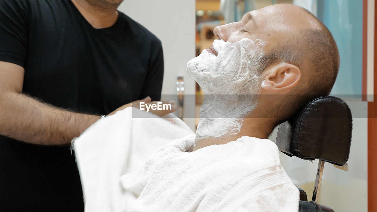 Barber applying shaving cream on mature man in salon