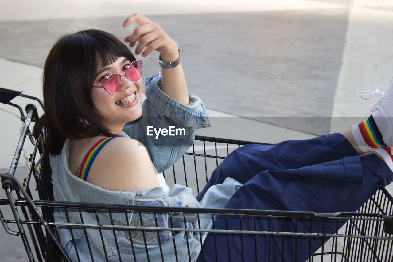 High angle portrait of smiling young woman sitting in shopping cart