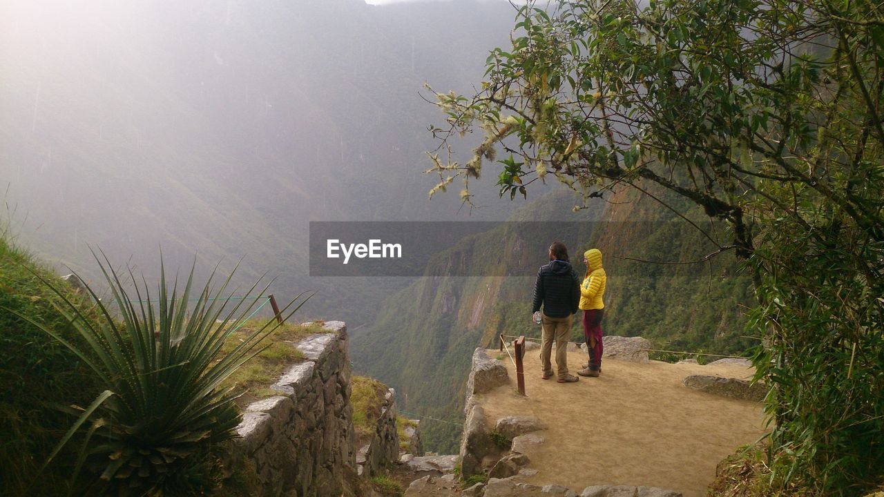 REAR VIEW OF MAN WALKING ON FOOTPATH BY MOUNTAIN