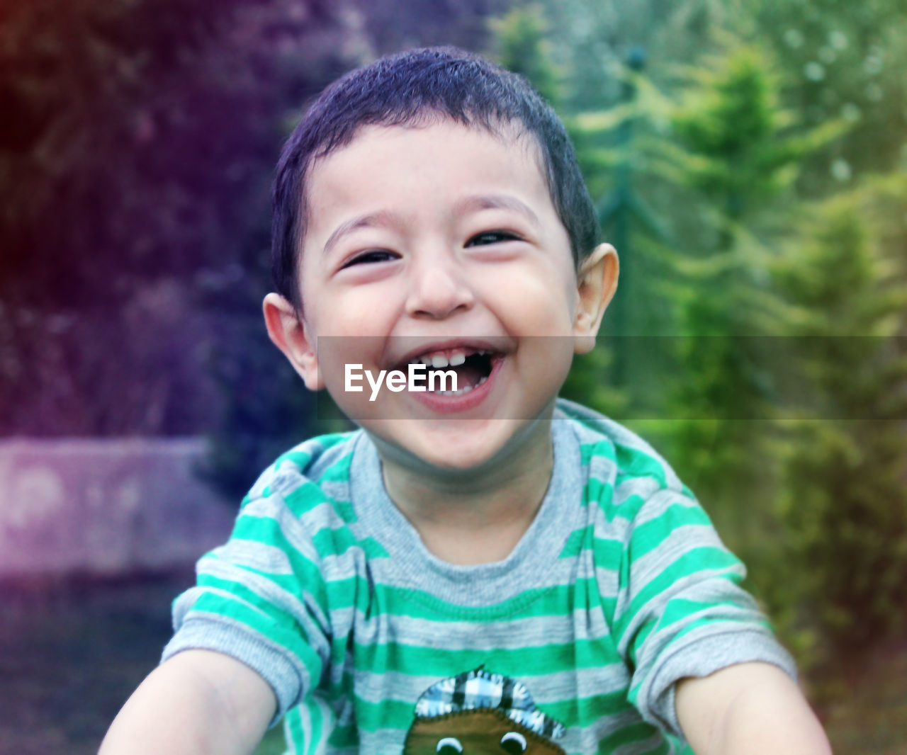 Portrait of cute boy laughing against trees