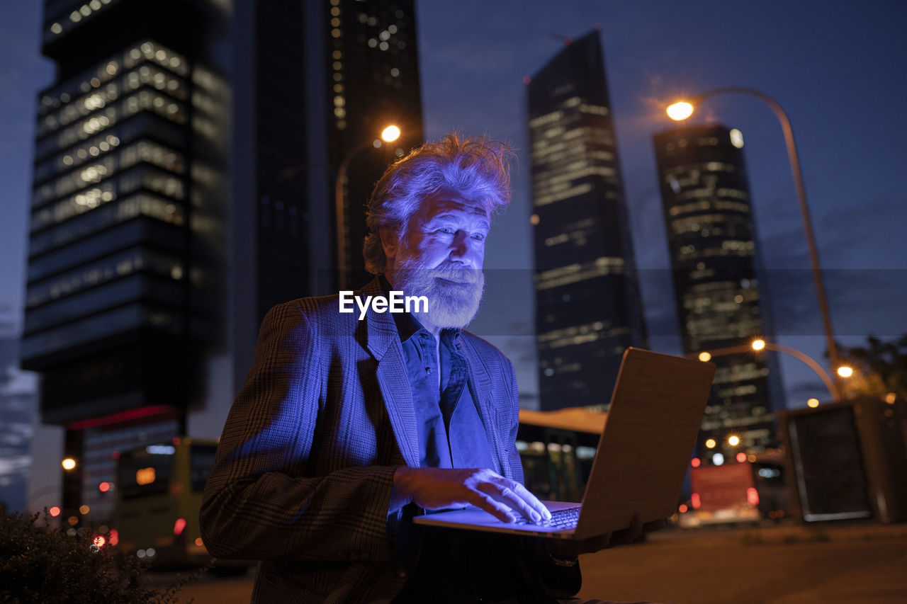 Male professional using laptop in city at night
