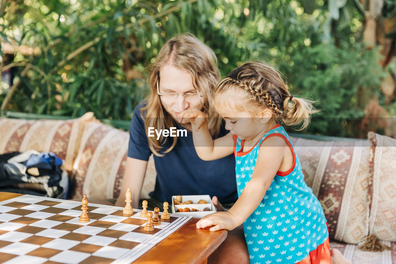 Girl standing by father arranging chess pieces on board