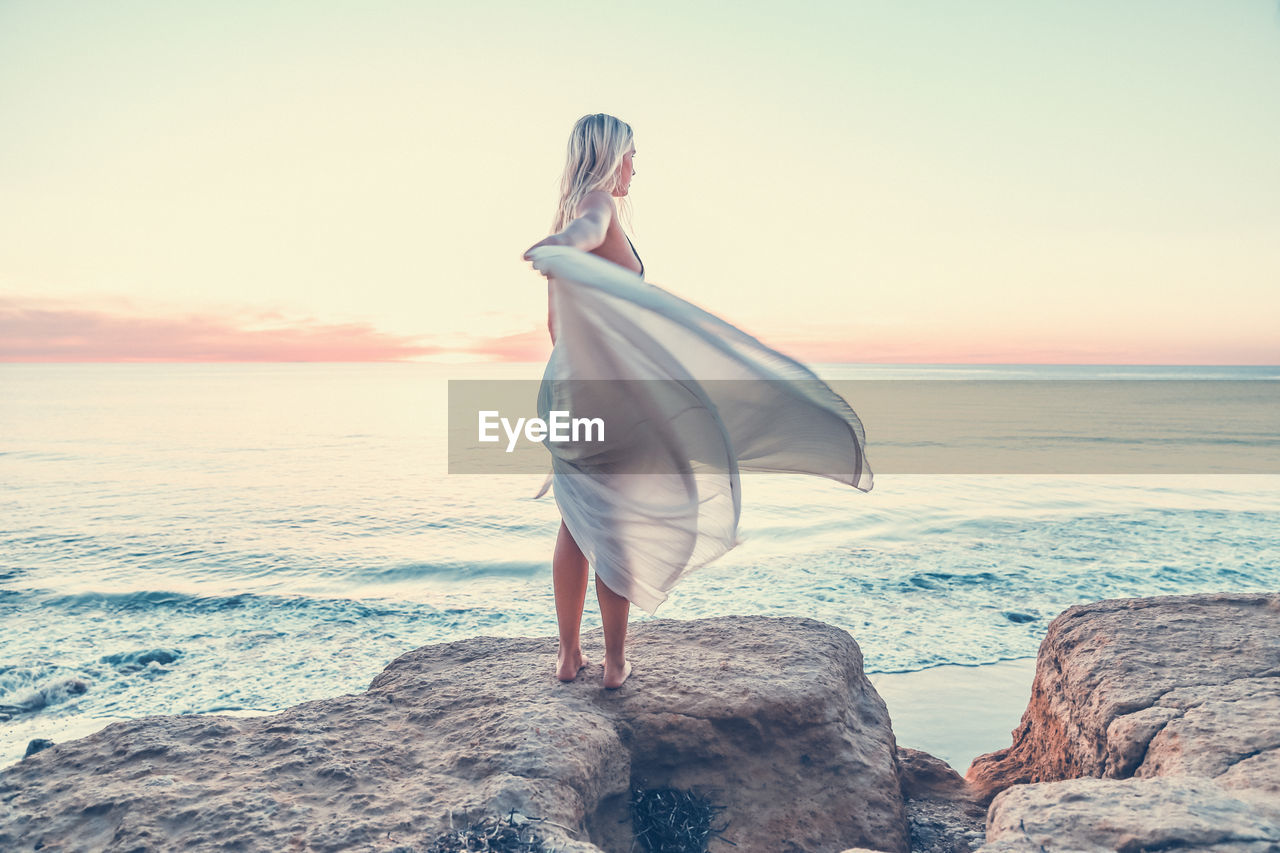 Rear view of woman with flowing white dress standing at beach.